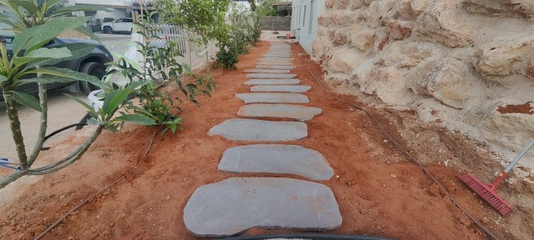 שביל גן עם אבני מדרך מלבניות גדולות על אדמה אדומה לצד סלעים